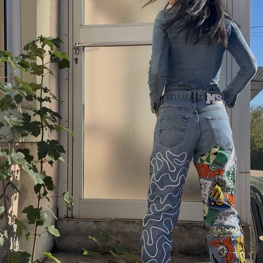 Dos d'un jean vintage taille haute avec une jambe en patchwork wax coloré et l'autre en denim brodé de surpiqûres blanches sinueuses